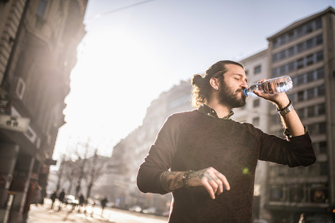 A tattooed man drinking water from a bottle.