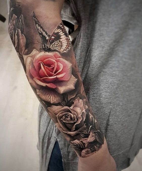 Tattoo sleeve with realistic roses and butterfly on an arm, showcasing detailed floral and insect designs on a grey shirt background.