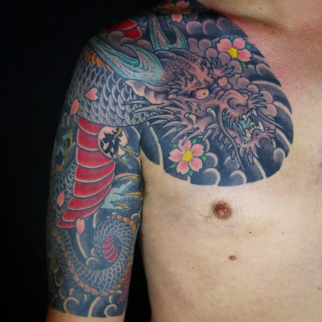 Dragon sleeve and chest plate tattoo with cherry blossoms by Kian Horisumi Forreal, showcasing the contrast between the dragon's strength and the cherry blossoms' gentle beauty.