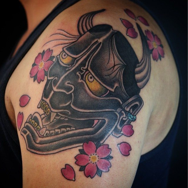 Hannya mask and cherry blossoms tattoo by Enku Shoji, showcasing the delicate beauty of sakura alongside a powerful traditional mask.