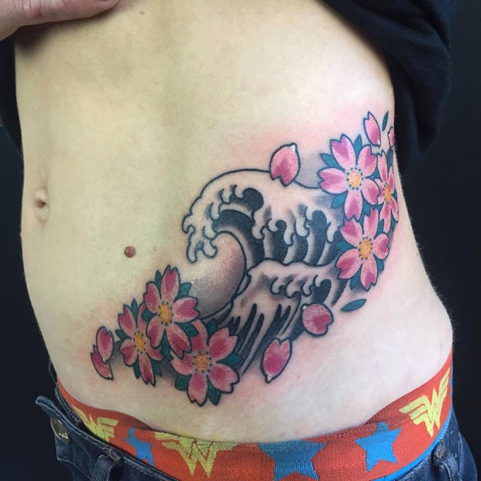 Rib tattoo featuring cherry blossoms and waves by Enku Shoji