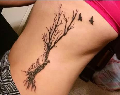 Tattoo of a tree branch with birds flying away, accompanied by the quote &quot;Still I Rise,&quot; representing hope and remembrance.