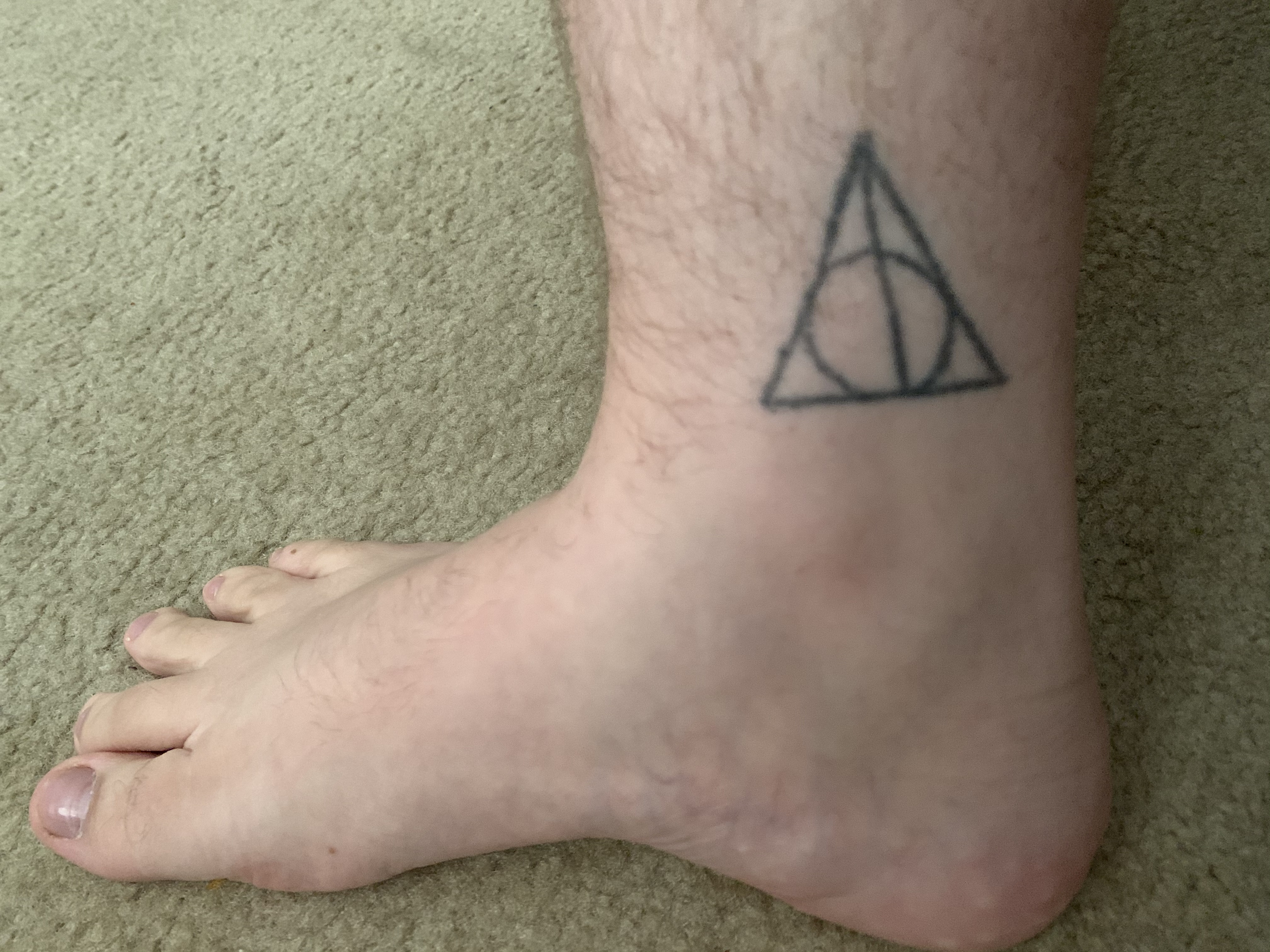 A stick and poke tattoo of the deathly hallows