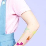 Close up of various glitter tattoo designs on arms, showcasing different colors and patterns.