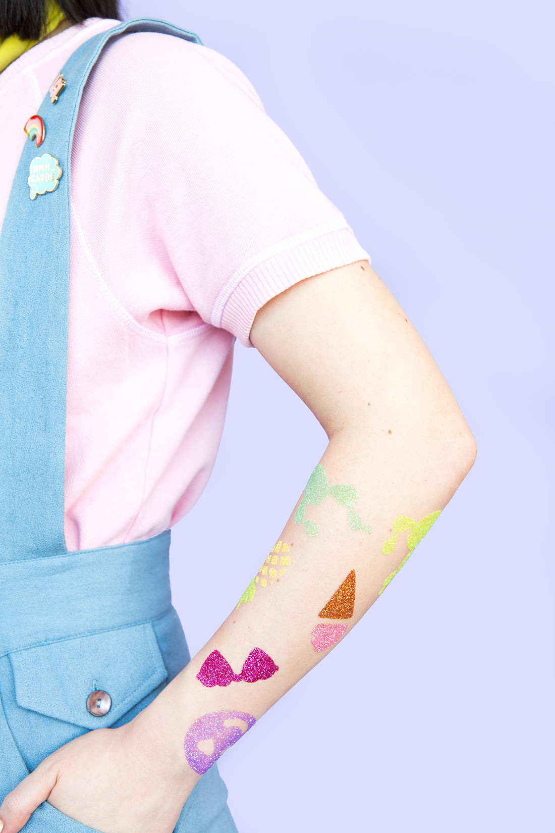 Close up of various glitter tattoo designs on arms, showcasing different colors and patterns.