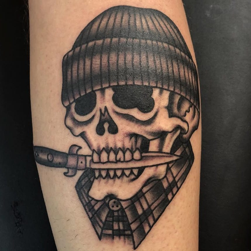 Tattoo by Ross K Jones. Traditional Chicano inspired tattoo by Ross K Jones featuring a skull, switchblade, and vato imagery in black and grey, blending traditional tattoo elements with Chicano themes in Ross K Jones's style.