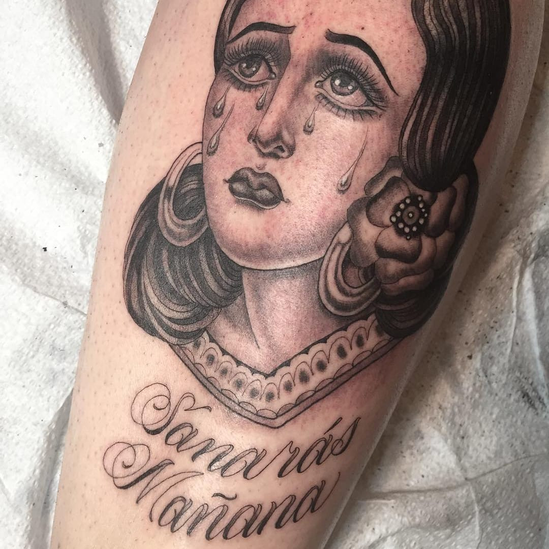 Tattoo by Tamara Santibanez. Intricate Chicano tattoo art by Tamara Santibanez featuring a portrait of a sad girl with tears, rendered in black and grey with fine line detail and script lettering, embodying classic Chicano tattoo style.