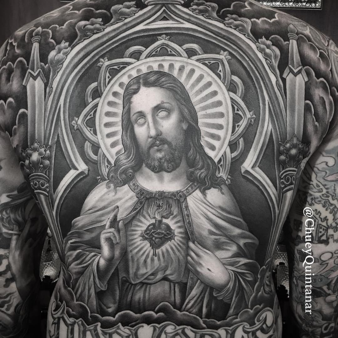 Tattoo by Chuey Quintanar. Reverent Chicano tattoo by Chuey Quintanar featuring Jesus Christ with a sacred heart in black and grey, demonstrating the religious themes and masterful black and grey technique in Chuey Quintanar's Chicano tattoos.