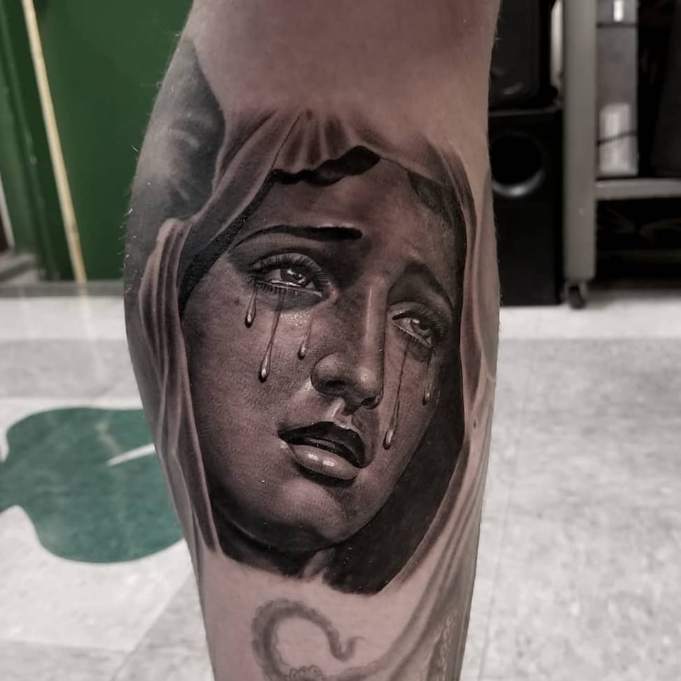 Tattoo by Freddy Negrete. Realistic Virgin Mary Chicano tattoo by Freddy Negrete with tears, rendered in black and grey, highlighting the realism and religious themes in Freddy Negrete's Chicano tattoo artistry.