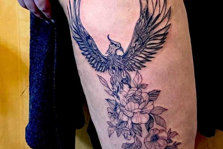 A delicate and feminine thigh tattoo of a phoenix intertwined with vibrant flowers, symbolizing the harmonious blend of rebirth, resilience, and natural beauty, perfect for expressing life's equilibrium.