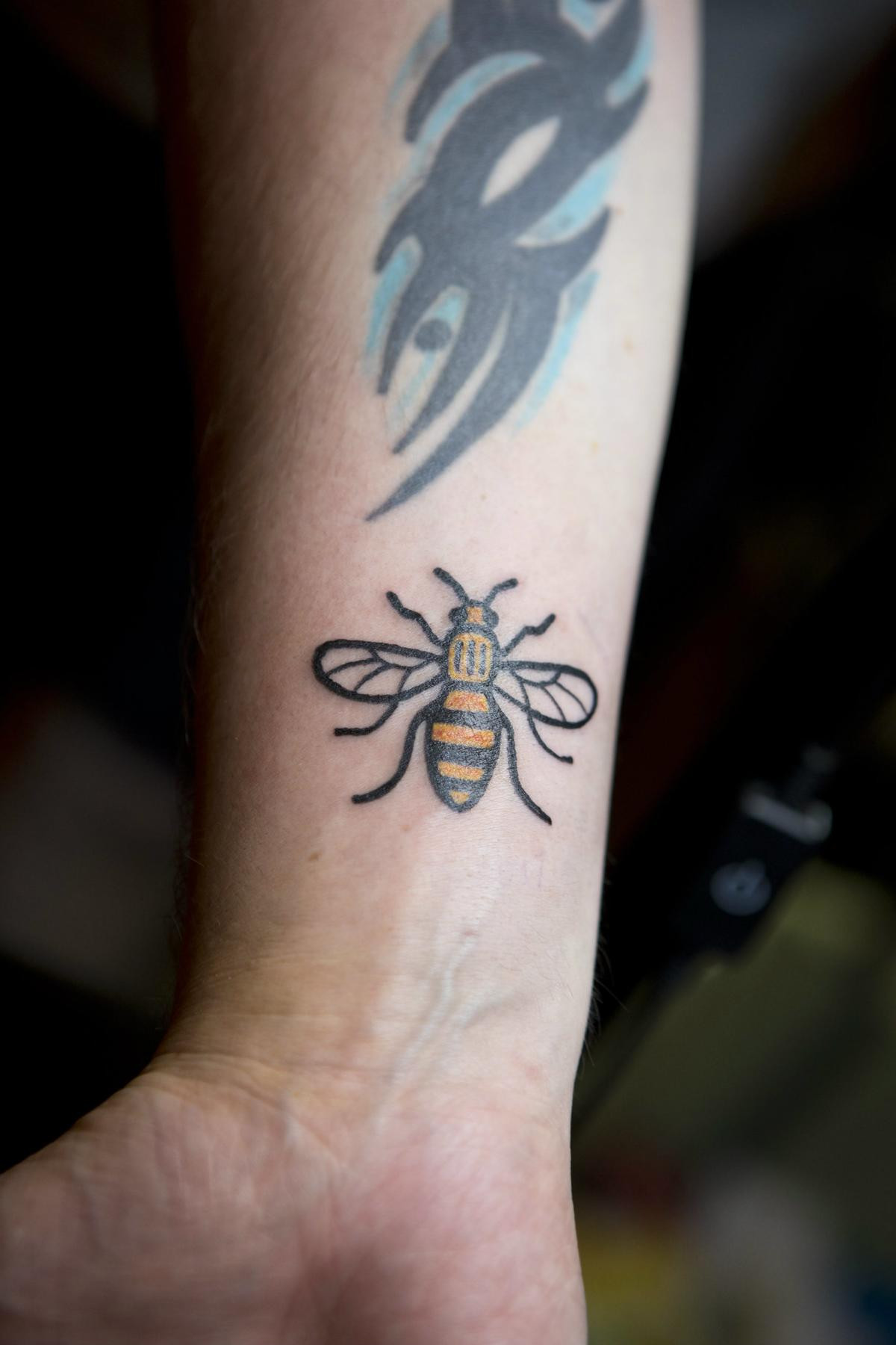 Close-up of a bee tattoo on a person's wrist, symbolizing personal connection to Manchester and community spirit.