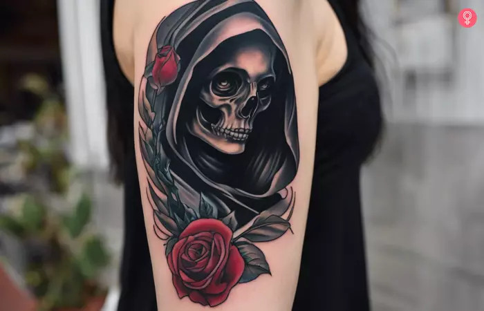 Traditional Grim Reaper tattoo on a woman’s upper arm, featuring a framed design with vibrant colors, roses, and striking contrast, representing the circle of life and beauty found within shadows.