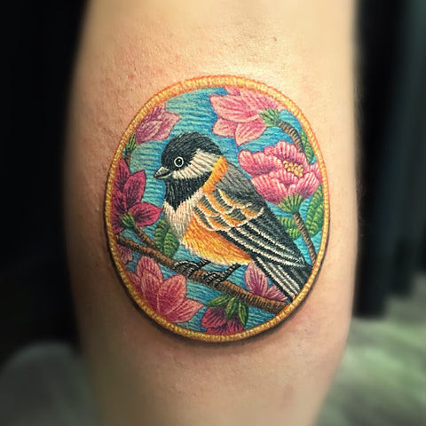 A vibrant hummingbird embroidered patch tattoo on an arm