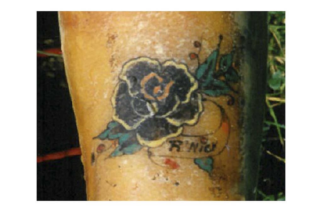 Close-up of the flower woman tattoo, showing the black flower, green leaves, and 'R'NICK' inscription.