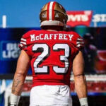 Close-up of Christian McCaffrey's arm tattoos featuring a lion, sword, compass, and mountain range.