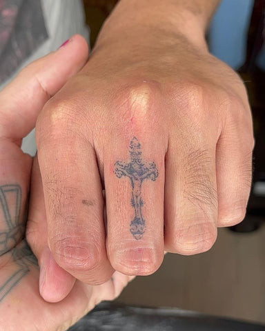 Minimalist cross finger tattoo on a man's hand, delicate and subtle.