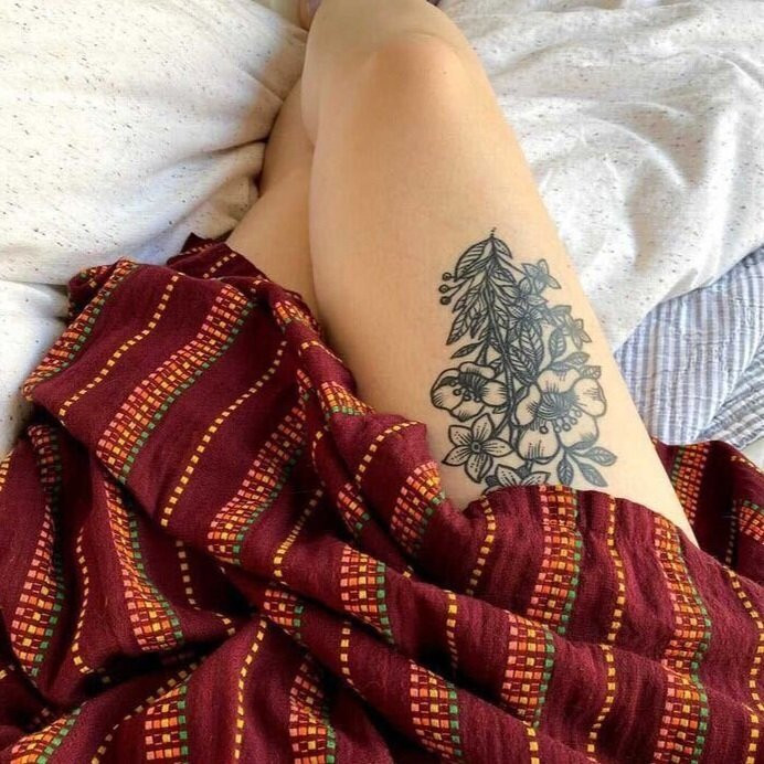 Close-up of Liz's arm tattoo, a colorful floral bouquet featuring calendula and poppies, symbolizing healing and resilience.