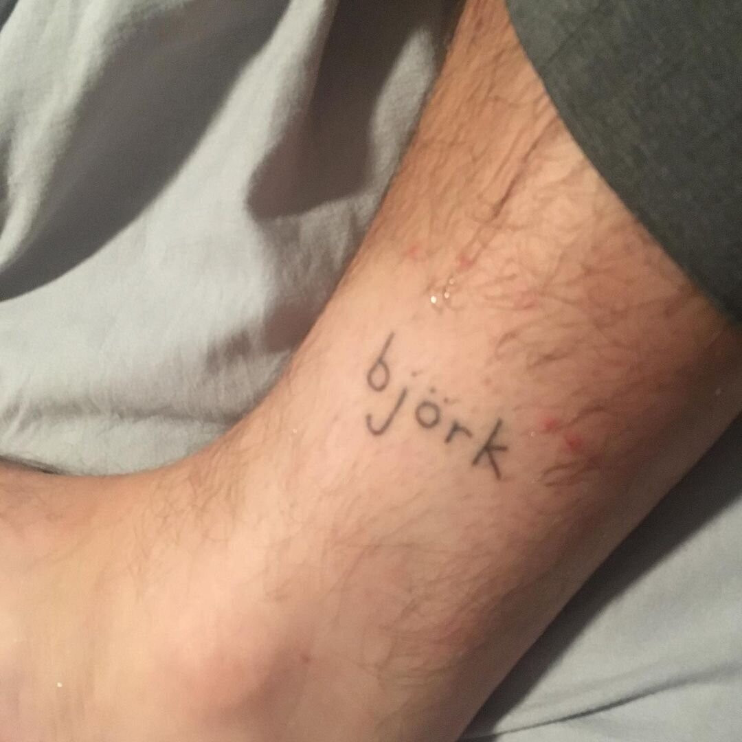 Close-up of Beau's ankle tattoo, the name &quot;Björk&quot; in simple stick-and-poke lettering, a tribute to her musical inspiration and personal hero.