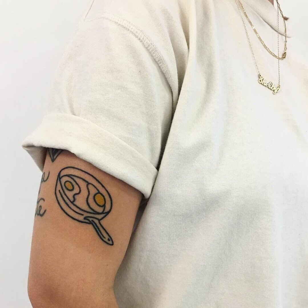 Close-up of Shelby's arm tattoo, a vibrant and stylized egg, based on a painting by her grandmother and appreciated for its novelty and personal connection.