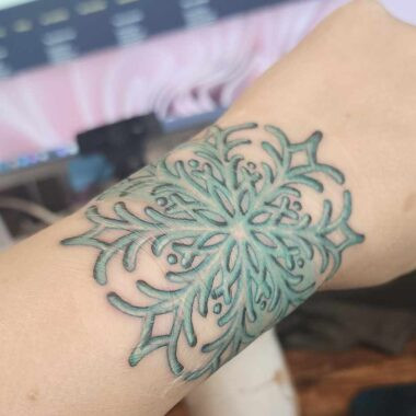 Teal snowflake tattoo on a light-skinned wrist.