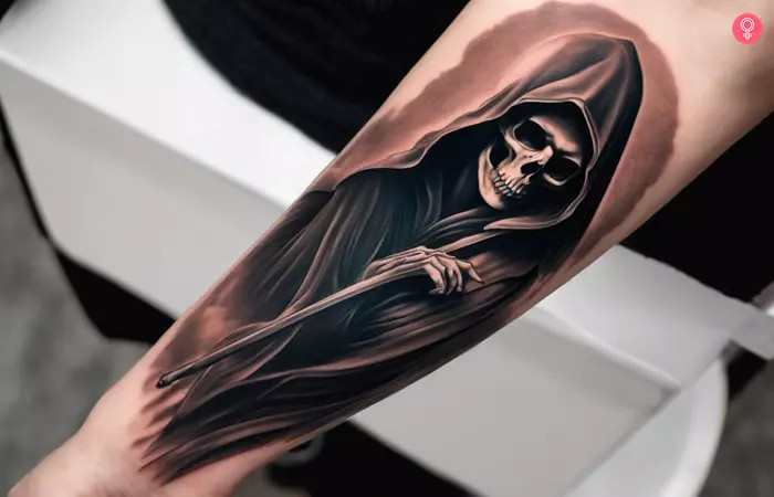 Forearm Grim Reaper tattoo, showcasing a reaper in a dark cloak with skeletal hands grasping a scythe, brownish shade, and eerie bony smile, symbolizing the frightful essence of death's arrival.