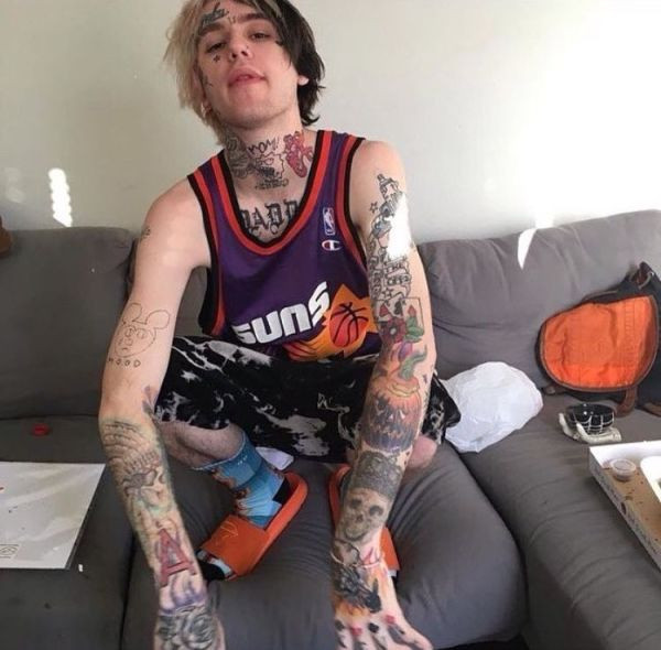 Lil Peep's arm and hand tattoos including Mickey Mouse, a native skull, &quot;A&quot;, a purple rose, playing cards, a poppy, a Halloween pumpkin, and a skull with a crown.