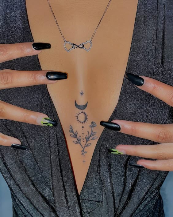 Stylish tattoo on chest with celestial design, black and green nails, and infinity necklace.