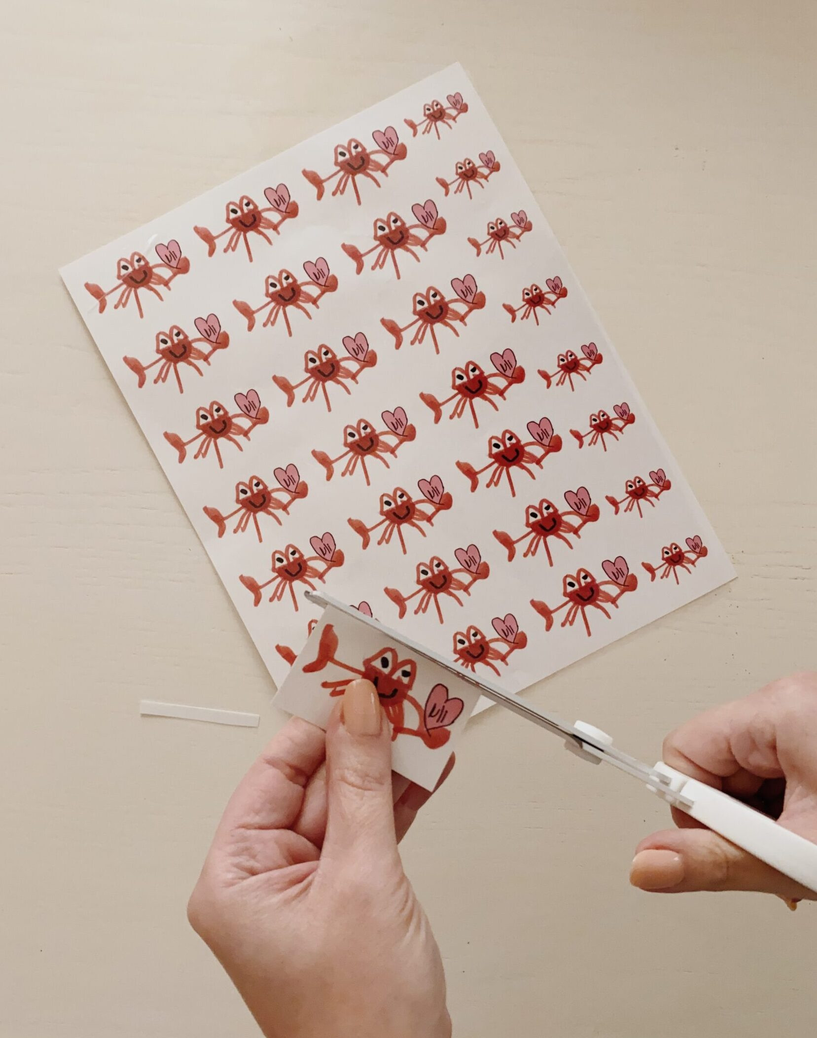 Applying the clear adhesive sheet to the printed tattoo designs and smoothing out air bubbles with a scraper tool, demonstrating the lamination process for temporary tattoos.