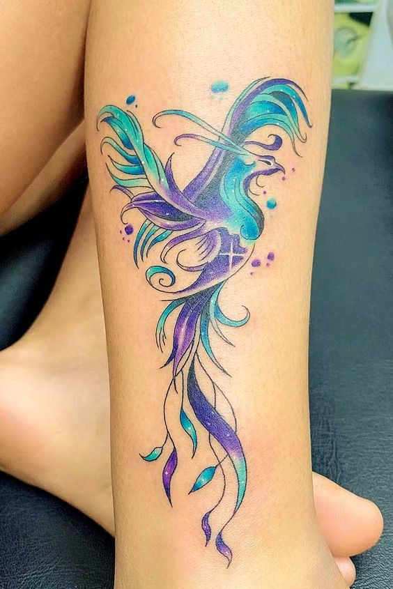 Colorful phoenix tattoo design on leg featuring vibrant blues, purples, and greens with intricate feather details.