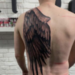 Detailed angel wing tattoo on a man's back, symbolizing freedom and guidance.