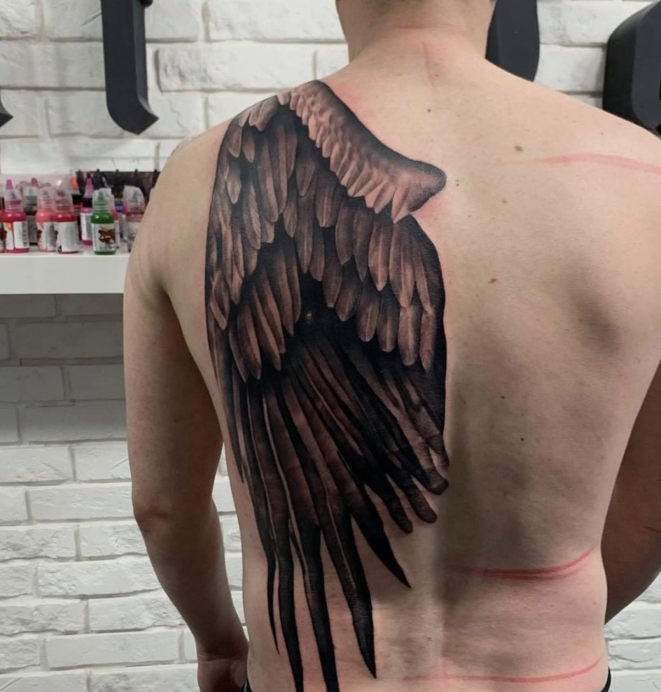 Detailed angel wing tattoo on a man's back, symbolizing freedom and guidance.