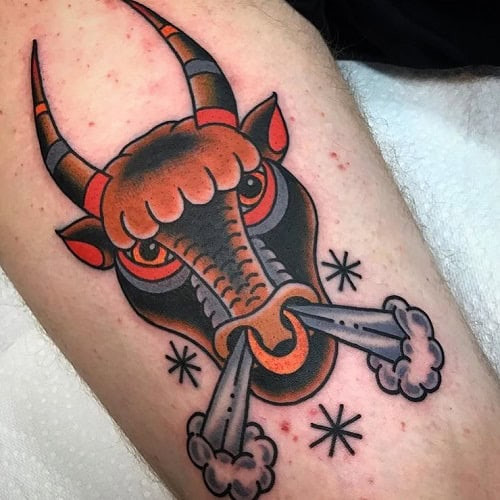 Angry bull tattoo in black and red ink with a fierce expression on the shoulder