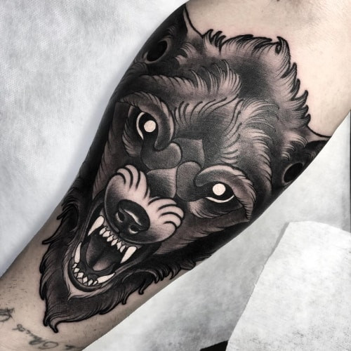 An angry wolf tattoo on a man's chest, depicting a snarling wolf face with intense red eyes, symbolizing fearlessness, strength, and bold emotional expression.