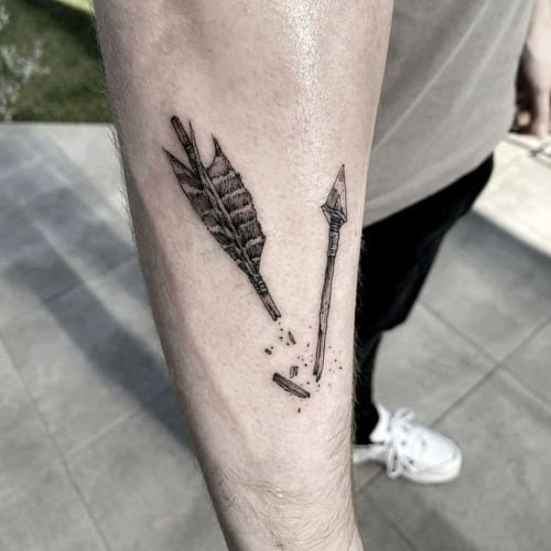 Two arrow tattoos on men, one on the wrist with a minimalist arrow outline and another on the forearm with a geometric arrow design.