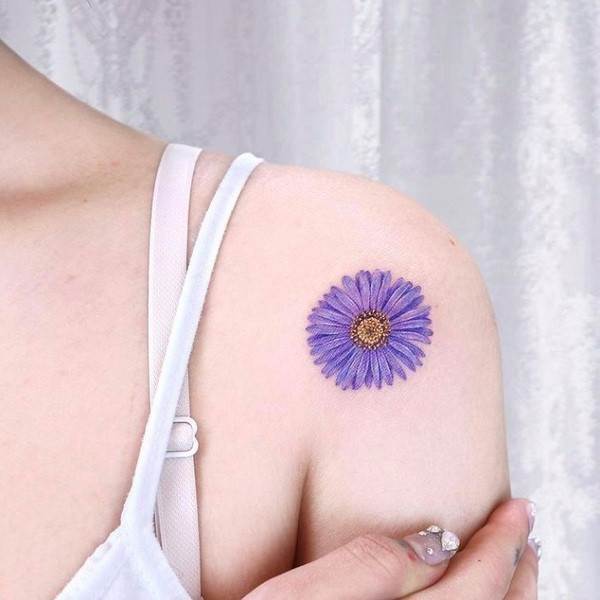 Detailed black and white aster flower tattoo on a forearm, showcasing delicate petals and shading.