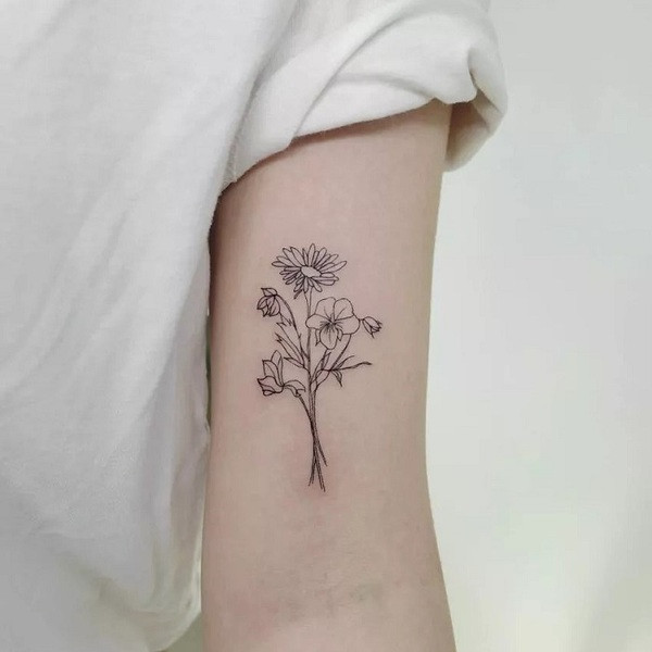 Single stem aster flower tattoo with delicate shading and fine lines, placed on the upper arm.