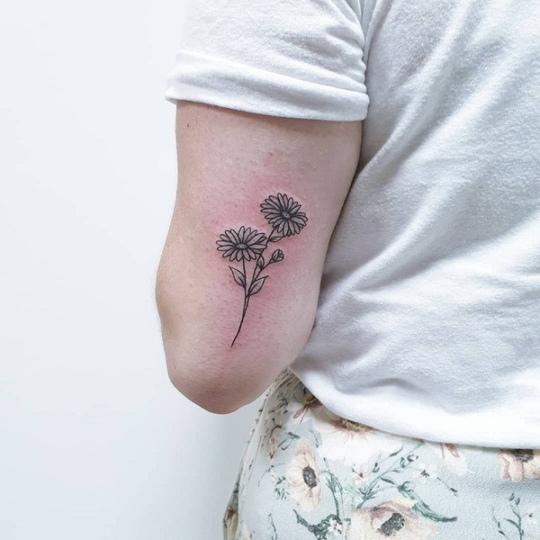 Geometric style aster flower tattoo using bold lines and dotwork shading, located on the forearm.