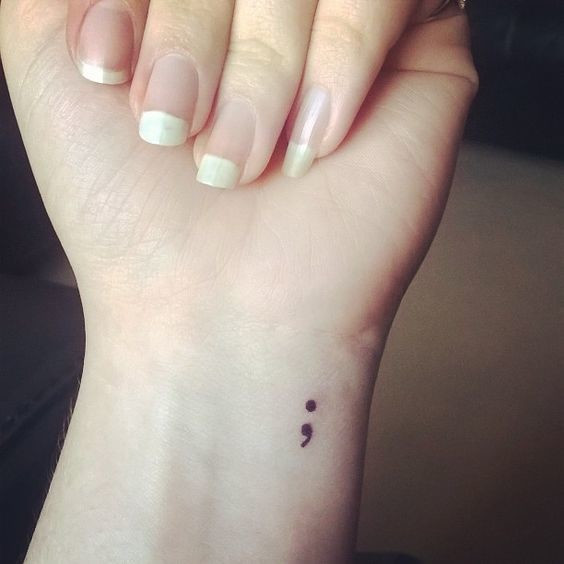 Simple semicolon tattoo behind the ear, a discreet yet powerful symbol of hope and continuation.