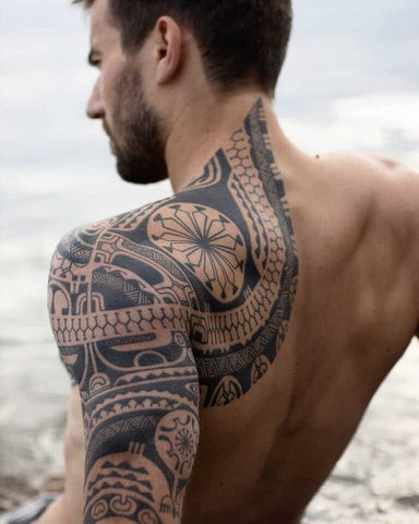 A detailed black and grey tattoo of angel wings spanning across a man's upper back and shoulders