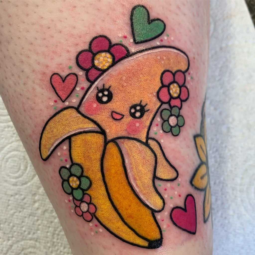 A cute banana tattoo with a smiling face, rosy cheeks, and bright colors, embodying playful and whimsical designs.