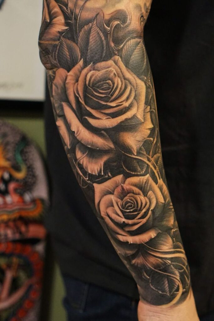 Realistic black and grey full-sleeve rose tattoo on arm featuring intricate details and shading.