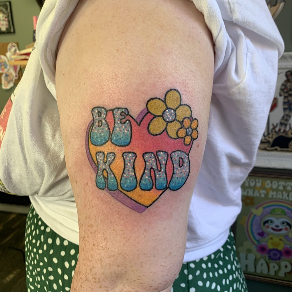 A cute and inspiring &quot;Be Kind&quot; tattoo in a whimsical style with pastel colors and gentle shading.