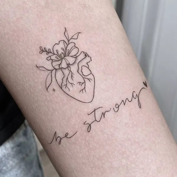 alt text: &quot;Be Strong&quot; script tattoo on forearm with floral accents, symbolizing healing, growth, and inner strength emerging from pain