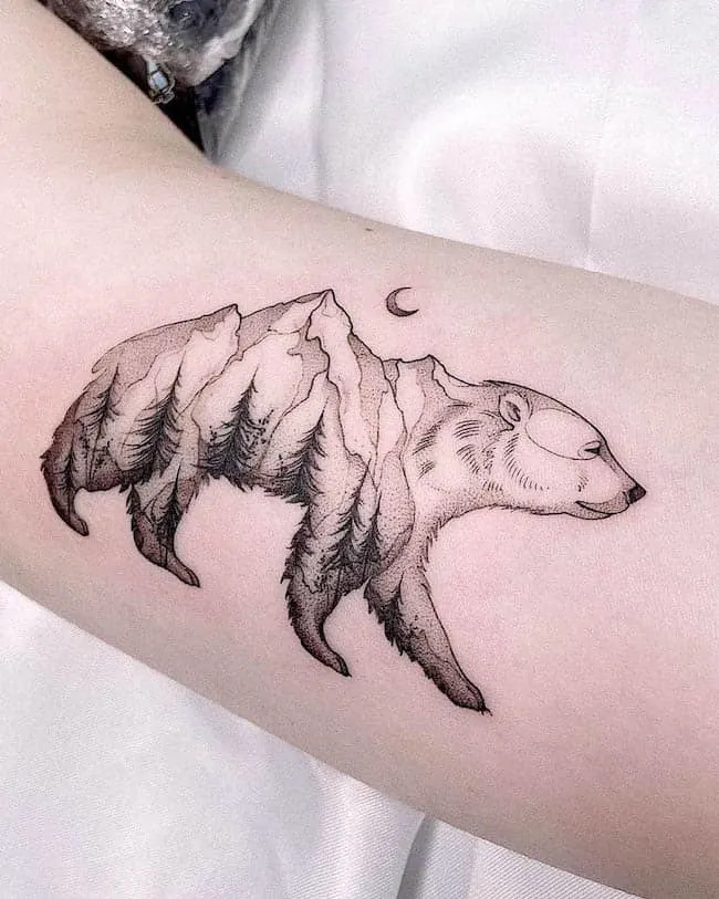 alt text: Detailed bear and mountain landscape tattoo on arm, symbolizing grounded strength, resilience, and connection to nature