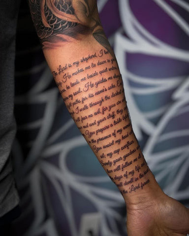 Detailed black ink Bible verse forearm tattoo in a calligraphic font, showcasing scripture as a source of inspiration and faith for men.