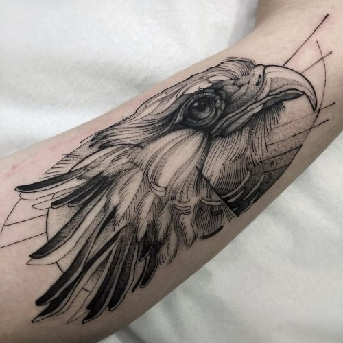 Two bird tattoos on men, one on the shoulder with a realistic detailed owl and another on the forearm with a geometric style bird in flight.