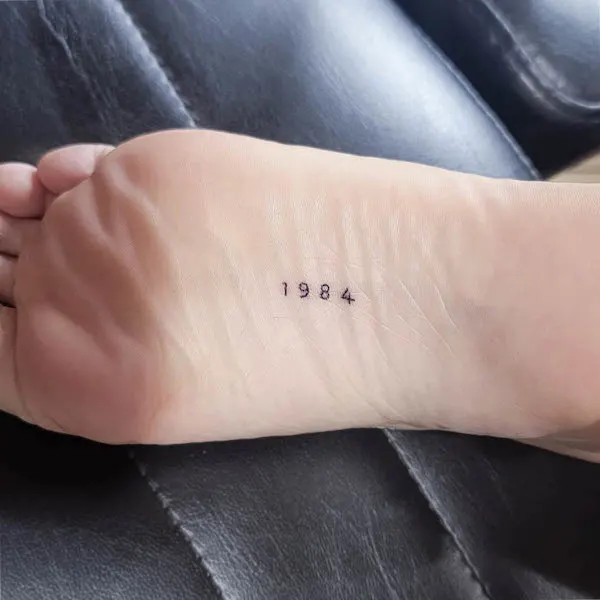 Birth of year foot tattoo, representing personal identity and gratitude for life, subtly placed on the bottom of the foot