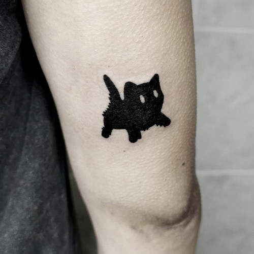 A small black cat silhouette tattoo perched atop a crescent moon, placed on the back of the neck.