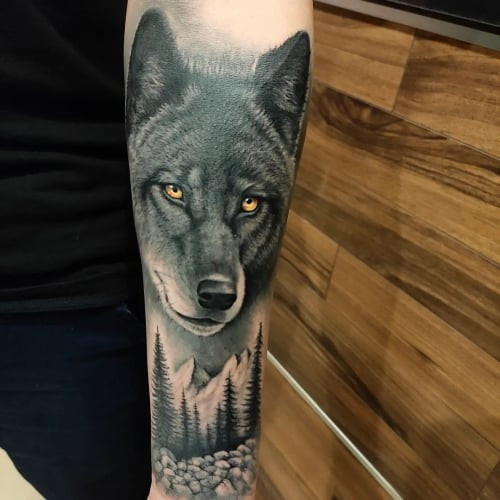A black wolf tattoo on a man's forearm, depicted entirely in black ink with varying shades to create depth and symbolism of inner strength, mystery, and the shadow self.