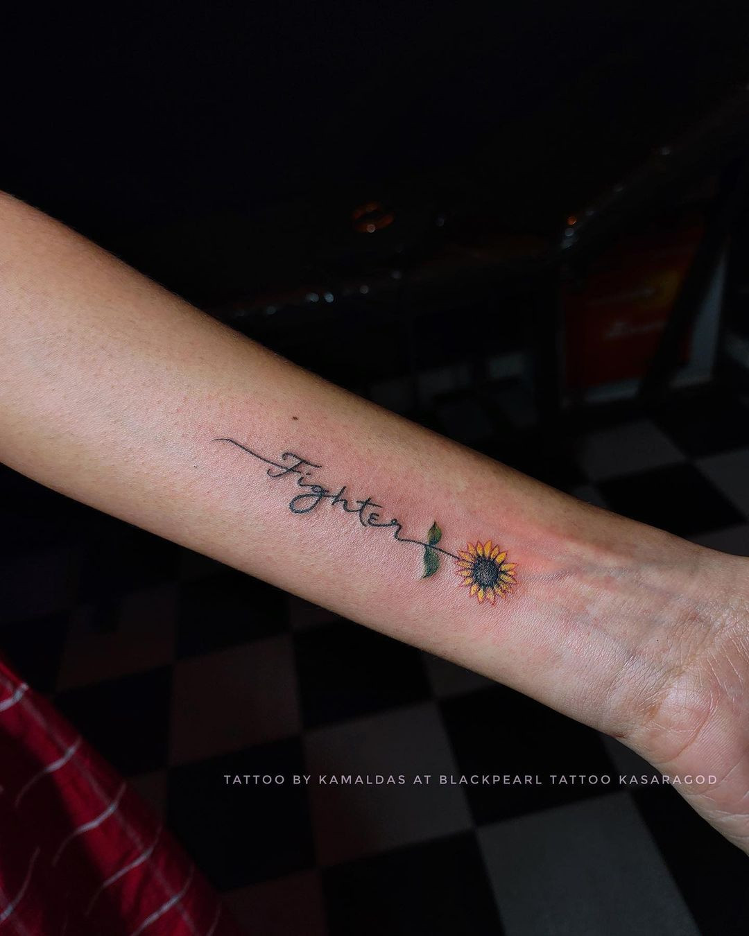 'Fighter' script tattoo with sunflower on forearm, motivational and floral detail